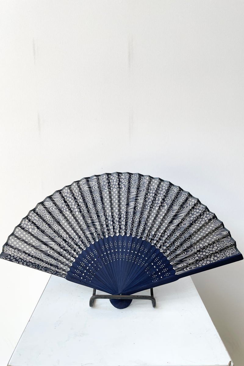 Blue bamboo and blue silk swirl pattern fan sitting open on a stand.