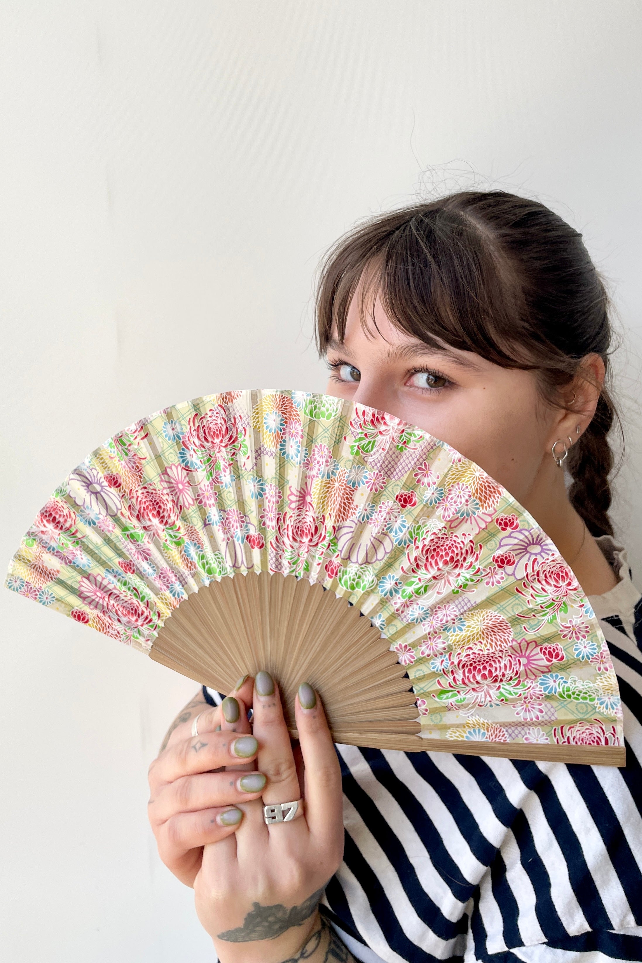 Pale green with Chrysanthemums silk fan being held in hand by a Sprout Home employee. 