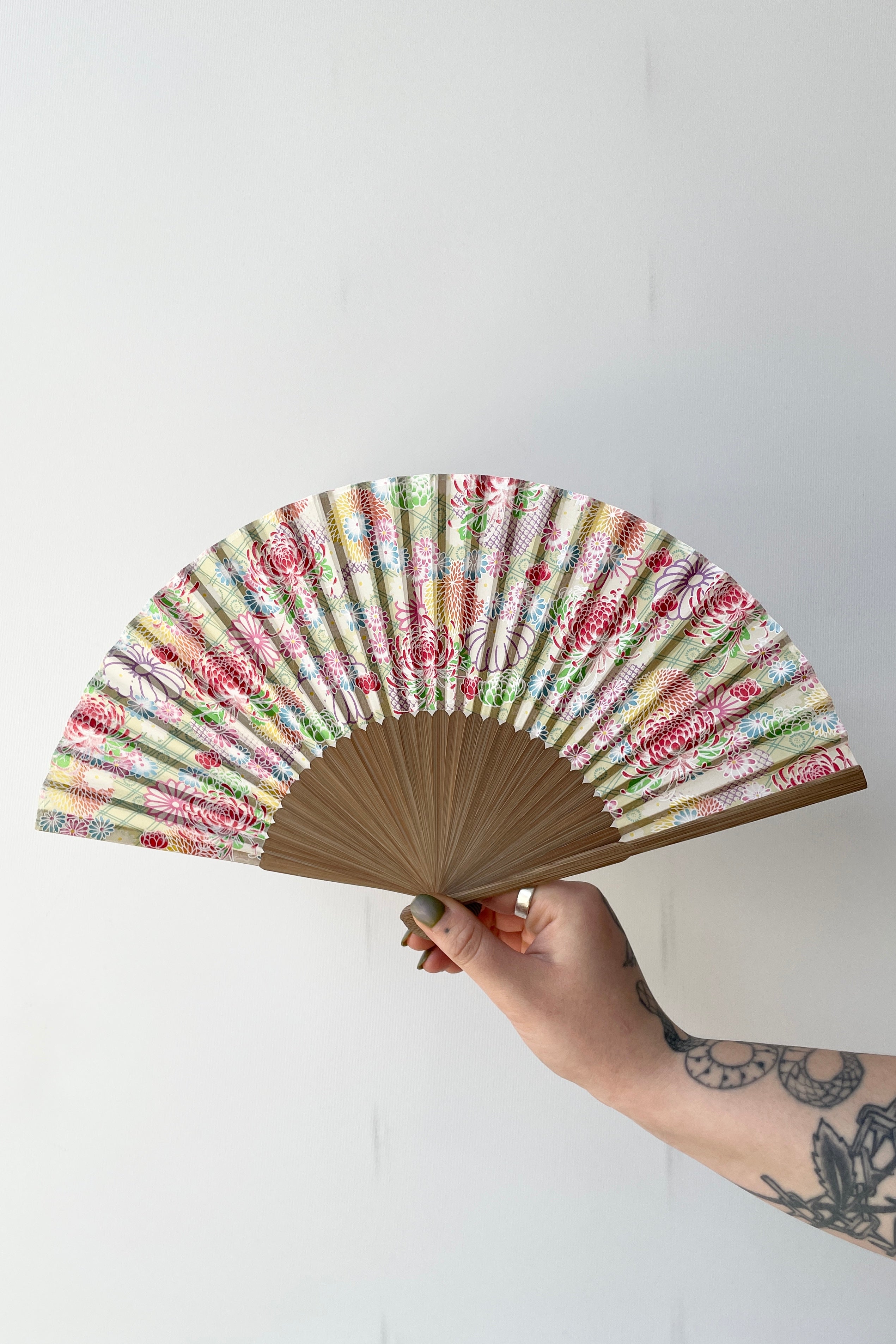 The slik fan pale green with chrysanthemums being held in hand against a white backdrop