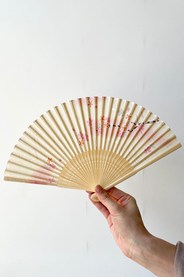 Silk fan with white and pink cherry blossoms being held by hand