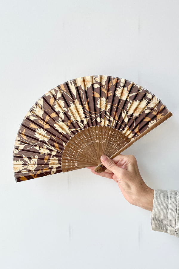 Silk fan brown flowers with brown bamboo being held in hand against a white wall