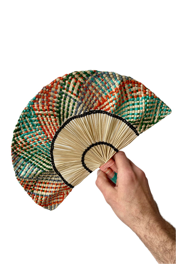 Toquilla Frilly Hand Fan Teal, Green & Red palm fiber on wire. This fan is held by a hand in front of a white wall.