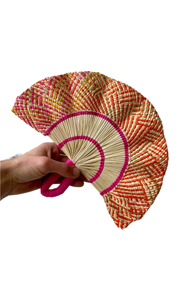 Toquilla Frilly Hand Fan Natural, Pink &Orange palm fiber and wire. A hand holds the fan in front of a white wall.