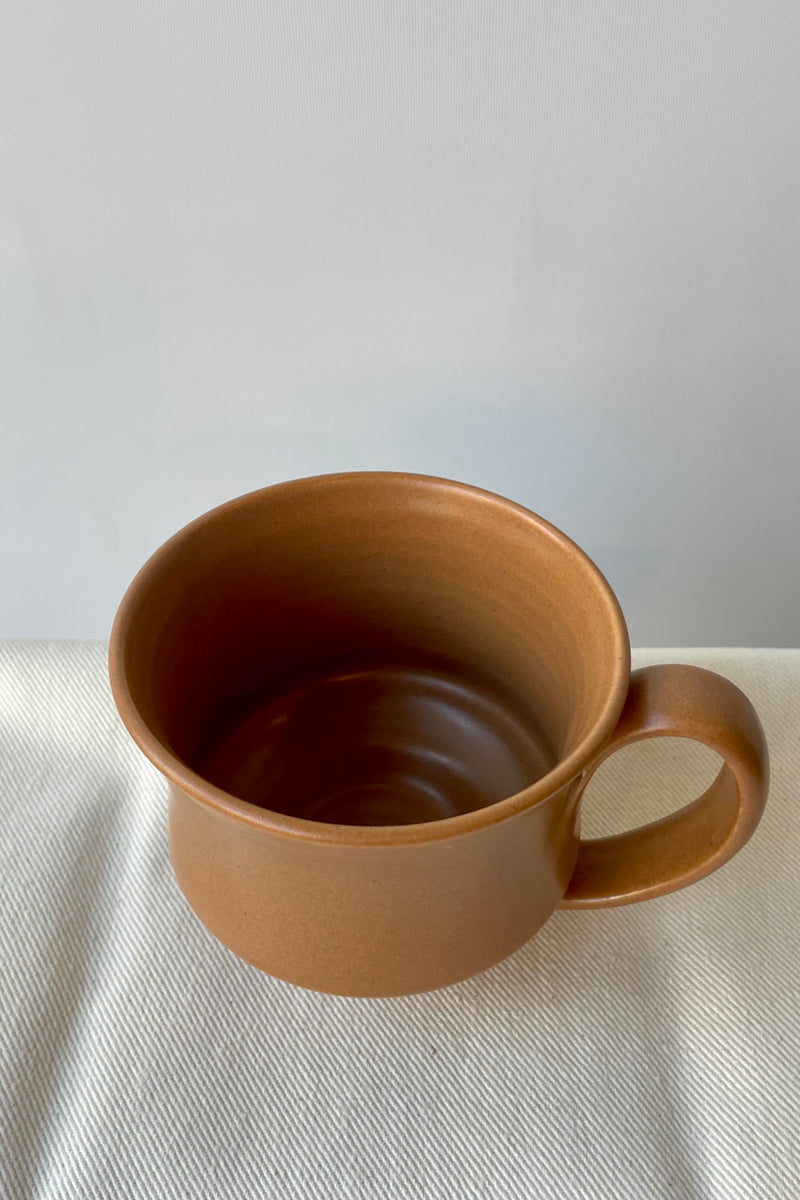 Photo of Little Fire Ceramics hourglass mug with caramel glaze. Shown from above. The mug sits on a white glass against a white wall.