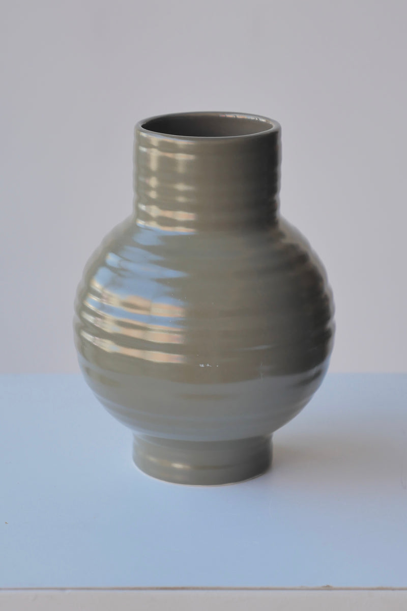 The Small Olive Essential Hawkins Vase against a white wall. 