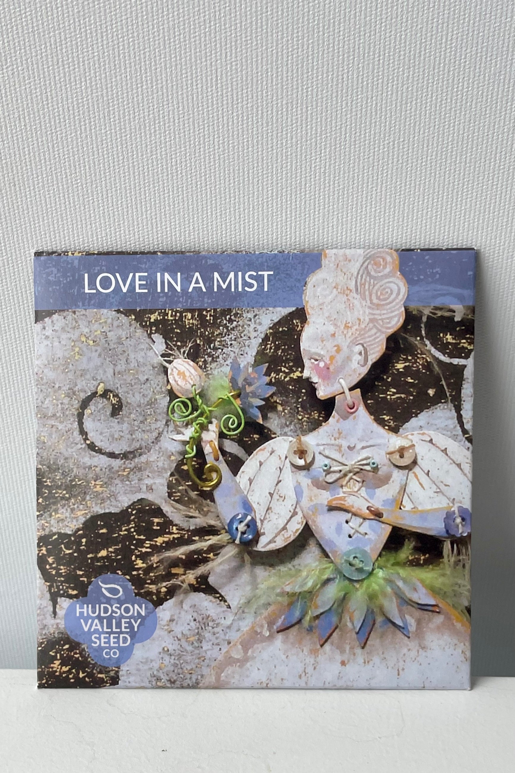 Packaging for 'Love in a Mist' seeds featuring an artistic depiction of the plant with feathery leaves and ornate flowers in shades of blue and white. ©Sprout Home