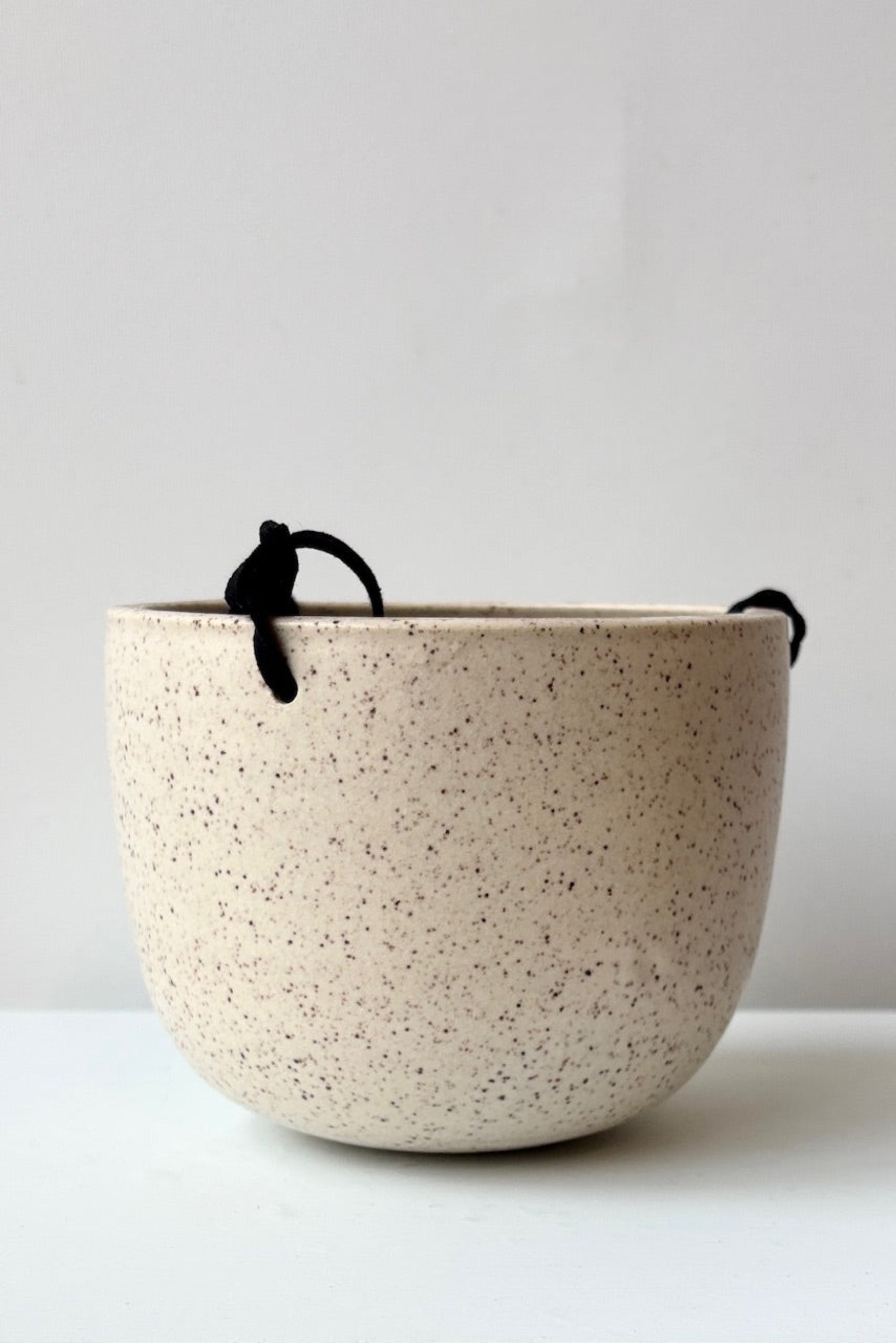 Speckled ceramic hanging planter with a black cord on a white background ©Sprout Home 