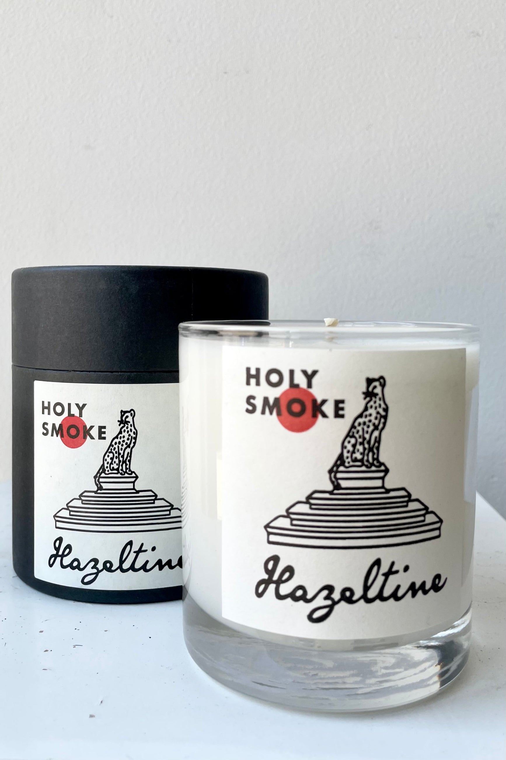 Hazeltine Holy Smoke candle showing the actual candle and the packaging box behind it.   ©Sprout Home