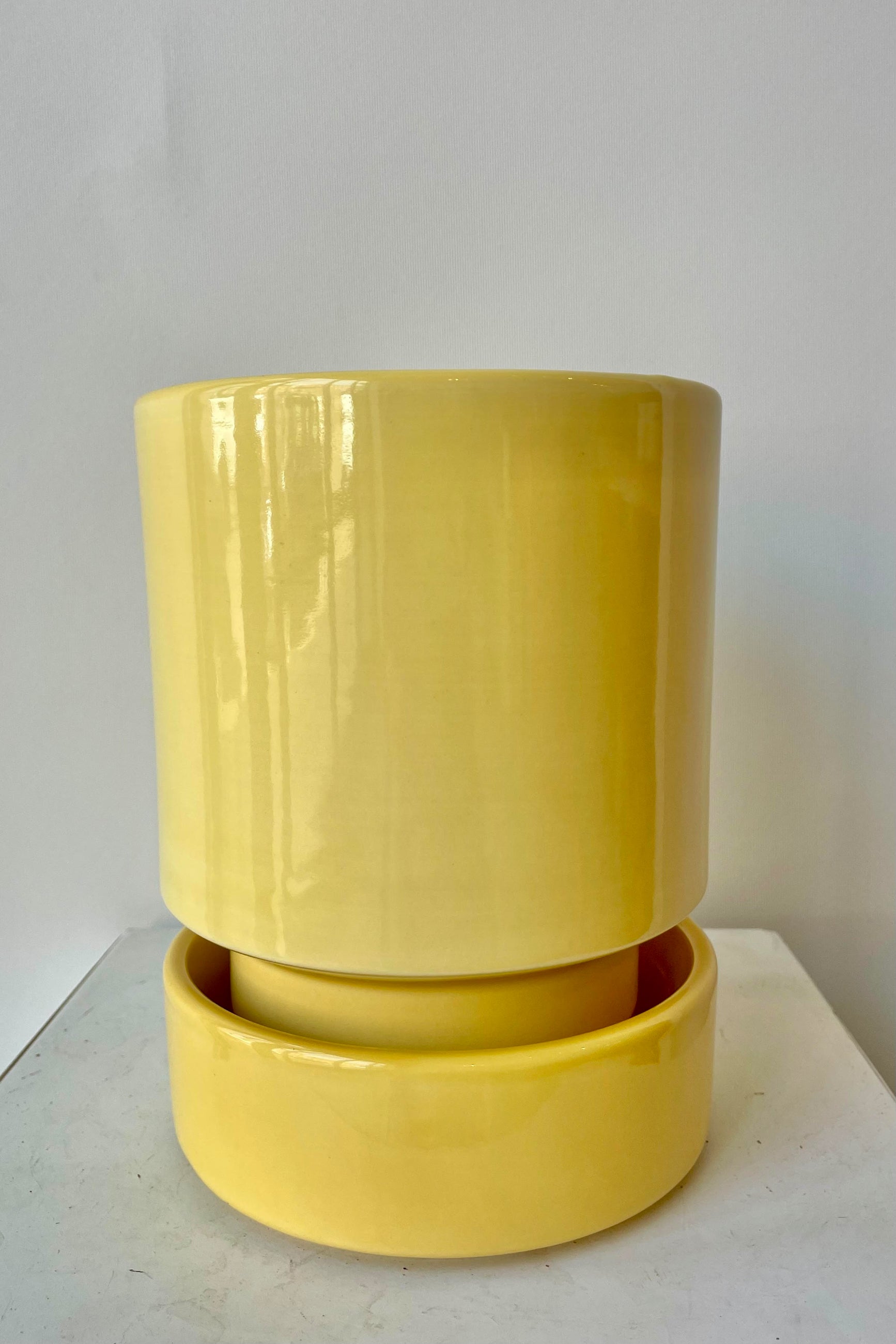 Photo of a Hoff Pot and Saucer set. The glaze of the pottery has a slight sheen and is a pale yellow in color. The pot sits within the deep saucer and the pair are photographed on a white surface in a white room. ©Sprout Home