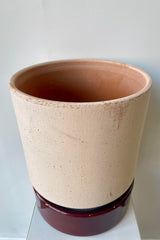 Photo from above of a Hoff Pot and saucer on a white table in a white room. The pot is rosa clay and sits within a deep burgundy glazed saucer.