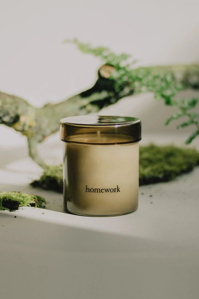 Wood candle outside of its packaging in front of a branch with moss by Homework