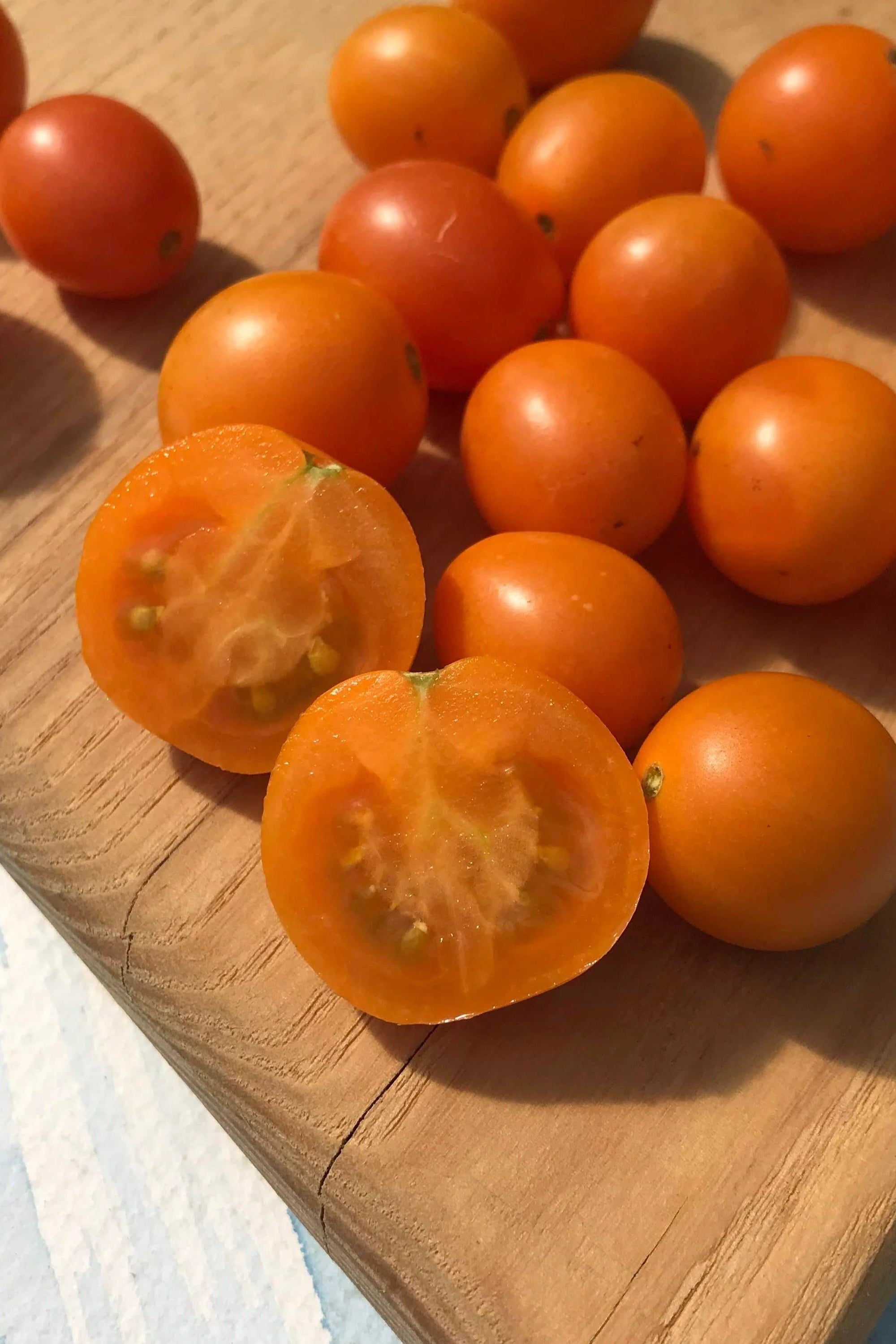 Small orange honey drop cherry tomatoes on a wooden cutting board ©Hudson Valley Seed Co.