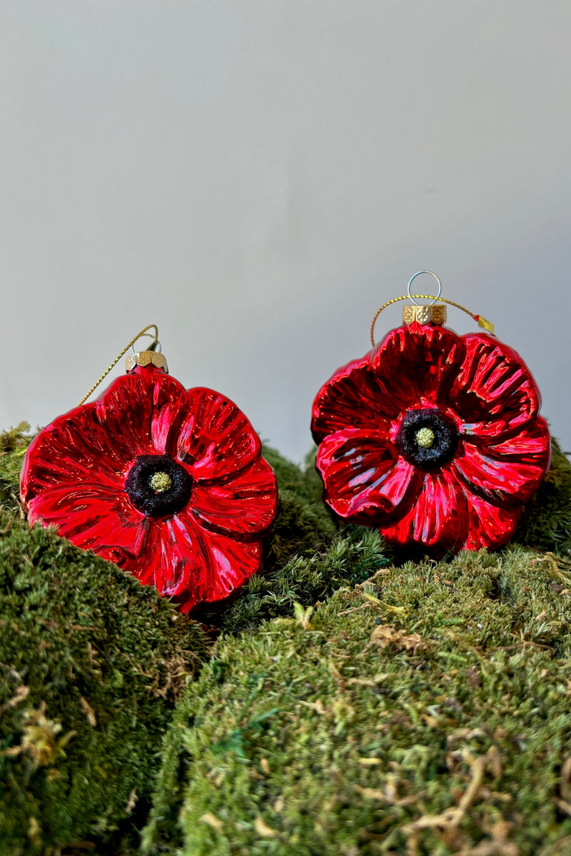 Glossy, bright red poppy ornaments with a black and yellow center displayed on a mound of moss against a white wall. 