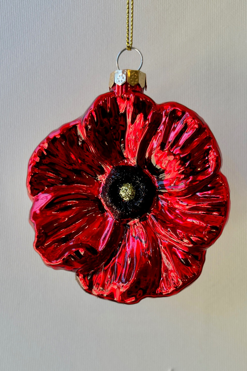 Glossy, bright red poppy ornaments with a black and yellow center displayed against a white wall.  ©Sprout Home