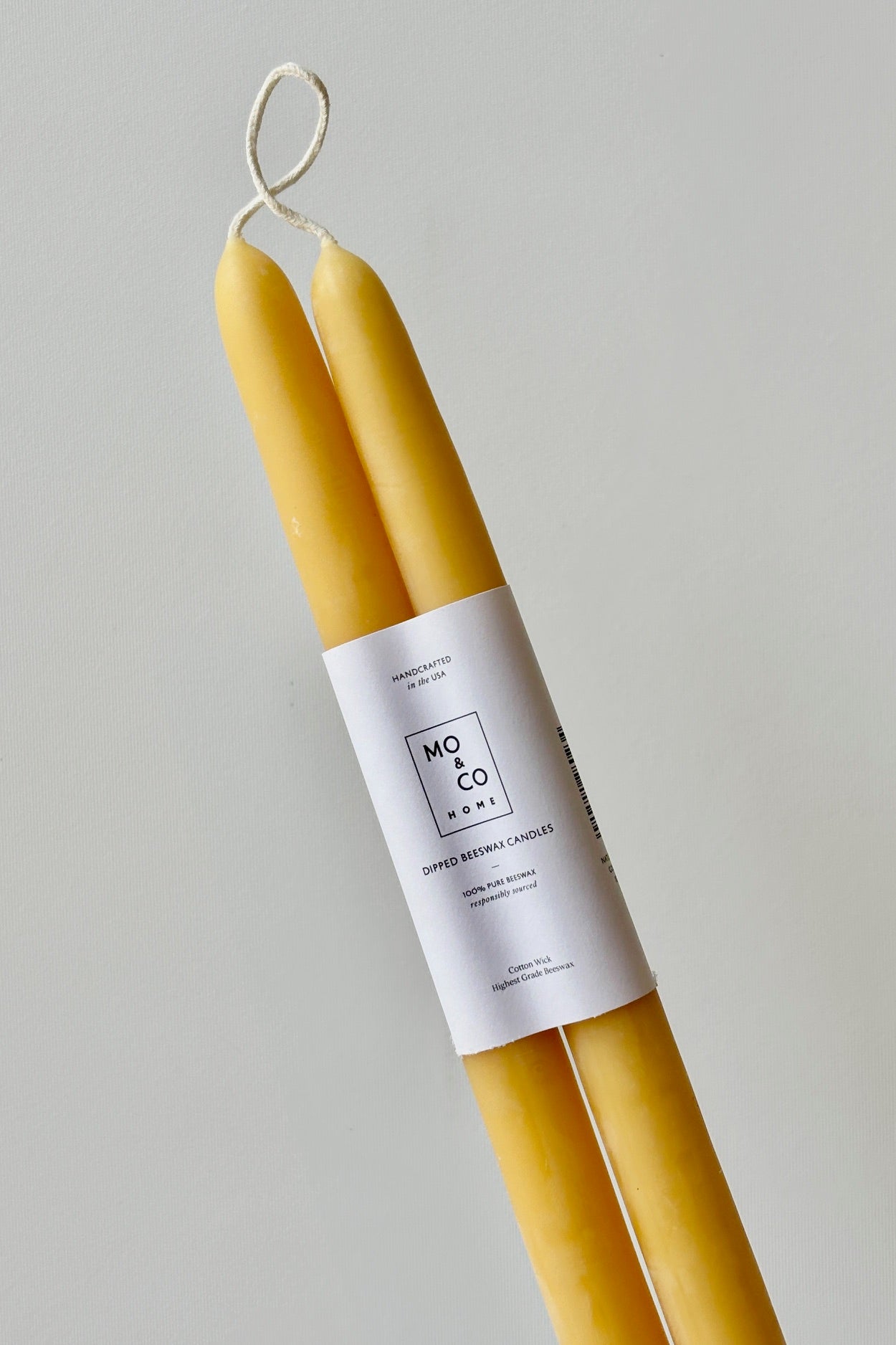 A pair of natural beeswax candles wrapped in a white label with the text Mo&Co Home on the front, against a white background.