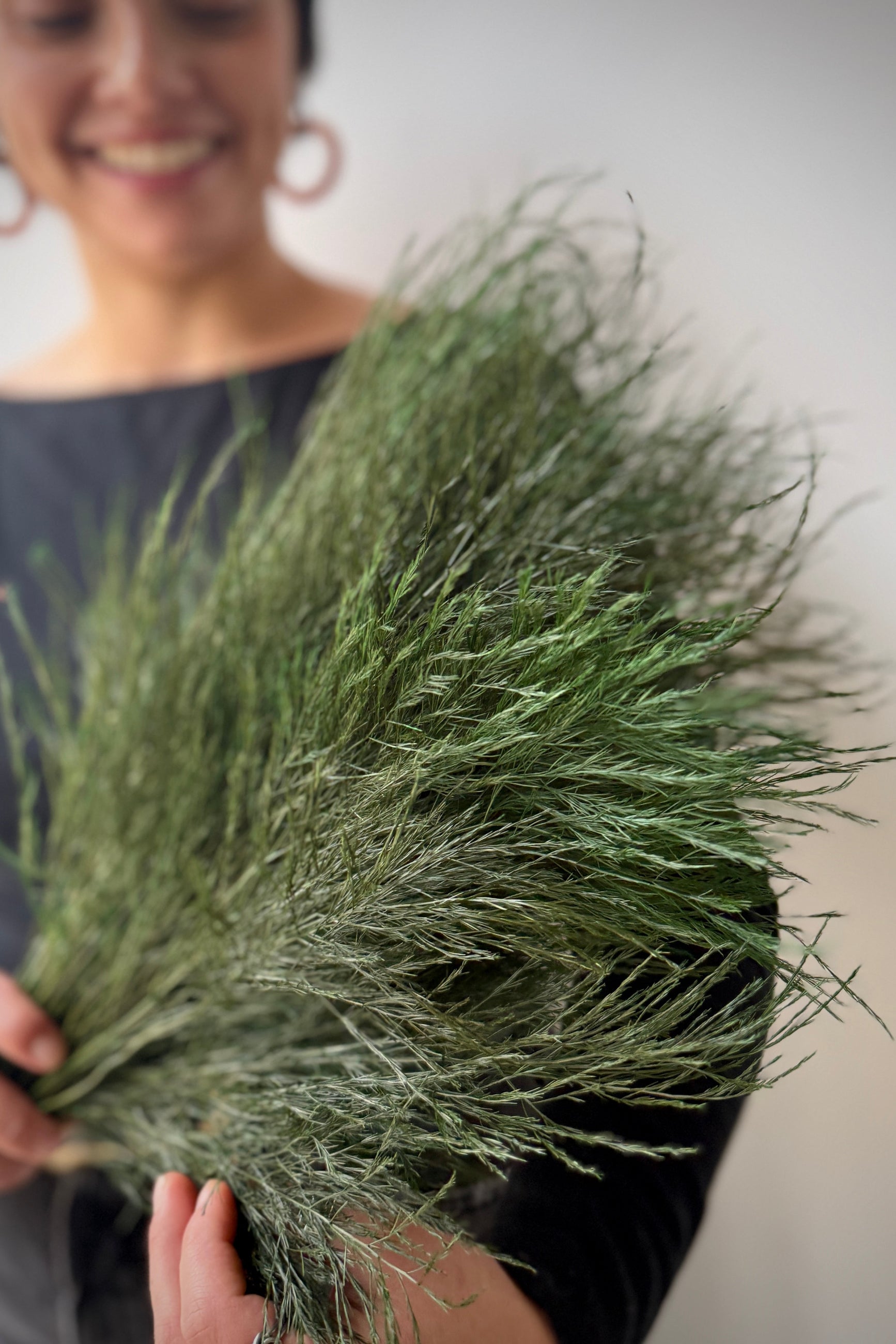 Sprout Home staff member  holding a bundle of preserved and dyed trifle asparagus fern against a neutral background ©Sprout Home