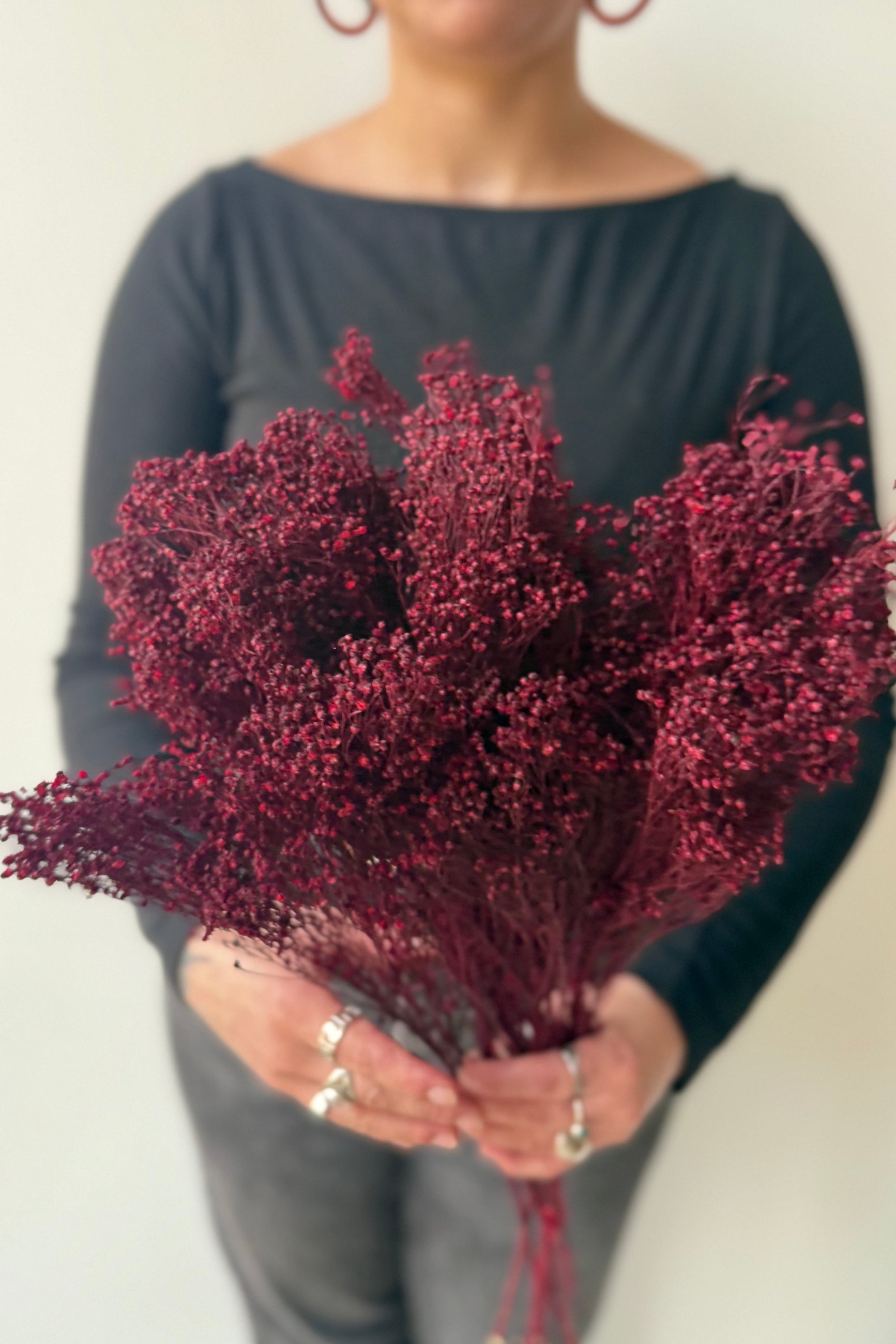 Sprout Home staff member holding a bouquet of burgundy dyed preserved dried flowers against a plain background ©Sprout Home