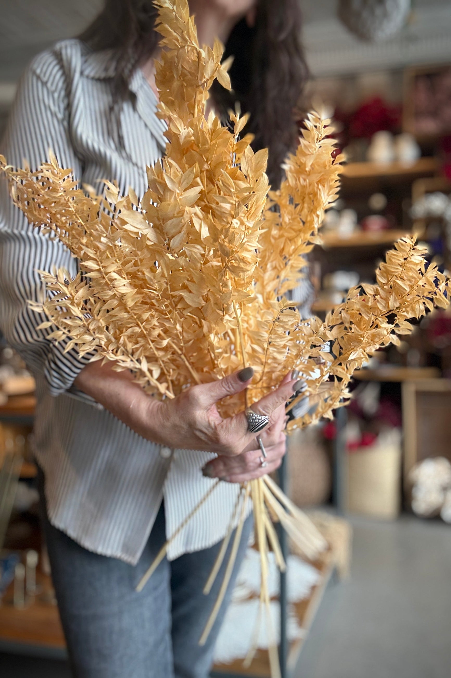 Tara holding a bouquet of dried and peach preserved Ruscus leaves in an indoor setting ©Sprout Home