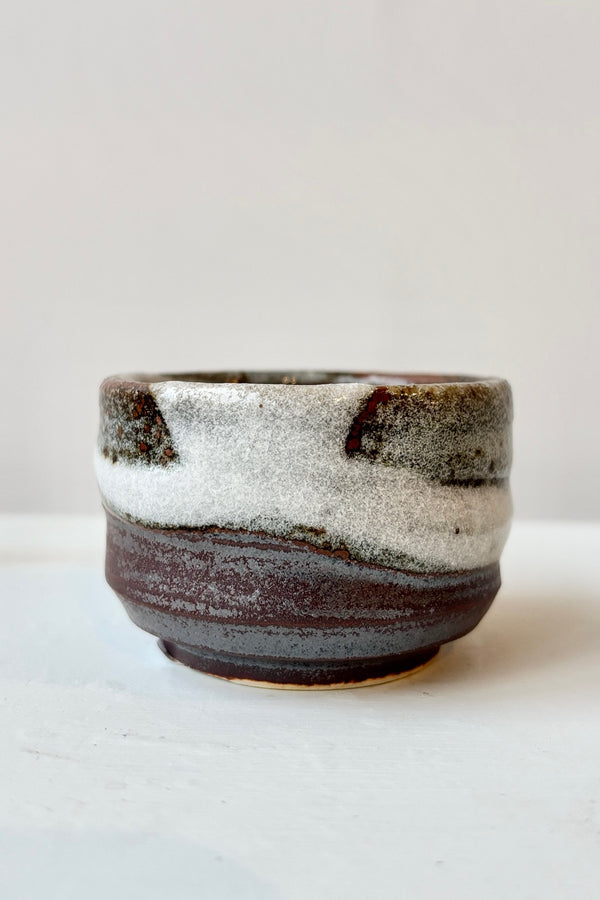 The Bizan sake cup with clay body and brown, white and gray glazing against white background.