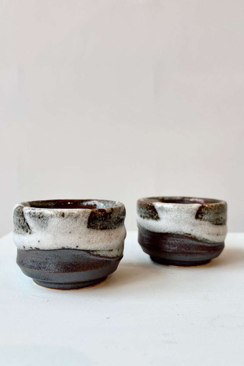 Two Bizan sake cups with clay body and brown, white and gray glazing against white background.