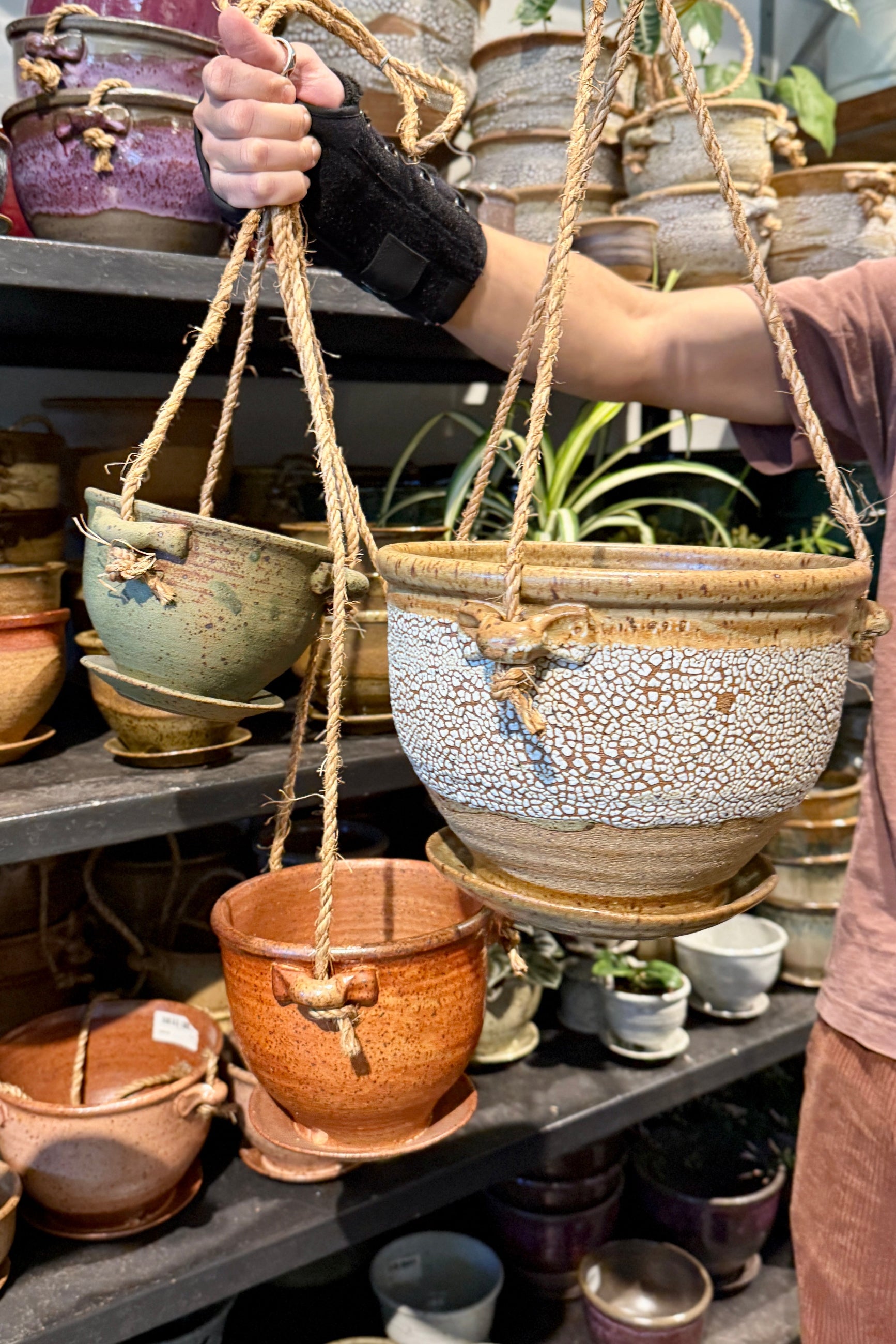 Person holding various Bruning Pottery hanging ceramic pot with a display of various Bruning Pottery pots in the background  ©Sprout Home