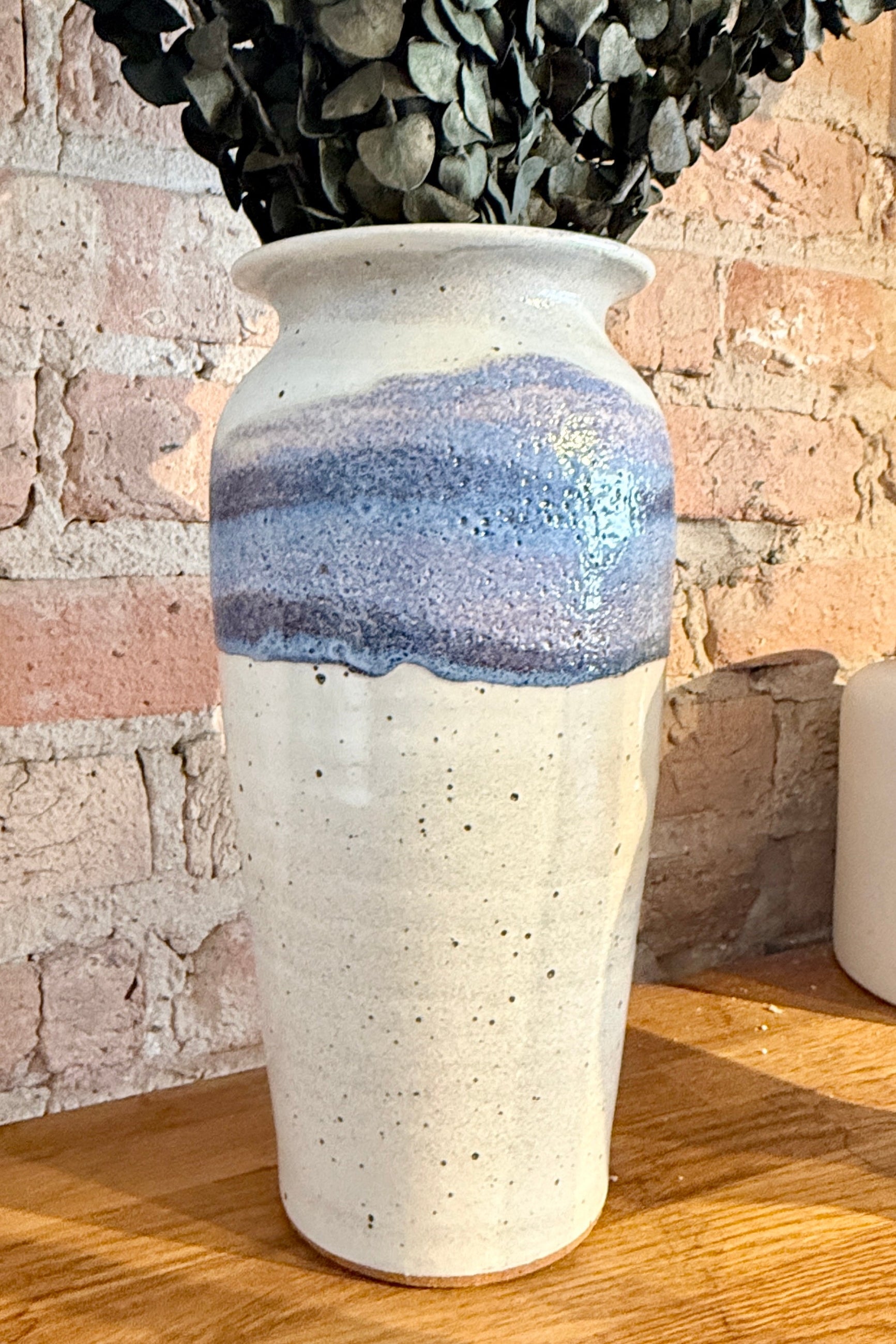 Bruning Pottery White ceramic vase with blue glaze on a wooden surface with a stone wall background ©Sprout Home