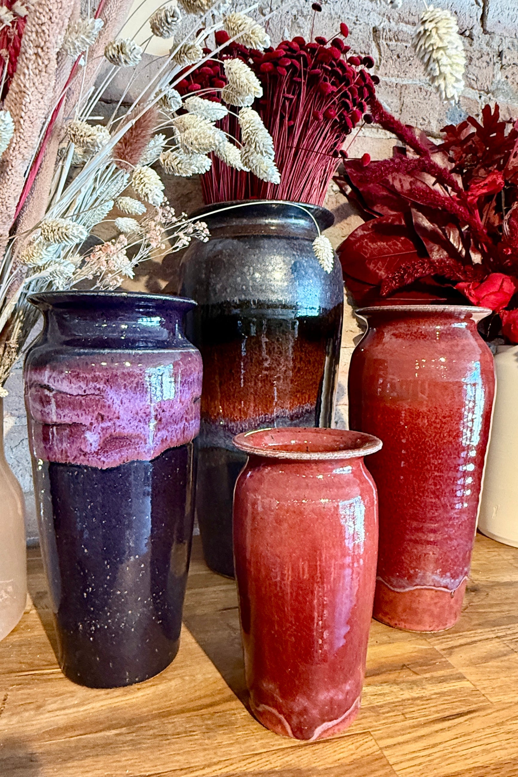 Set of four Bruning Pottery ceramic vases in various shades of red and brown on a wooden surface with dried flowers in the background. ©Sprout Home