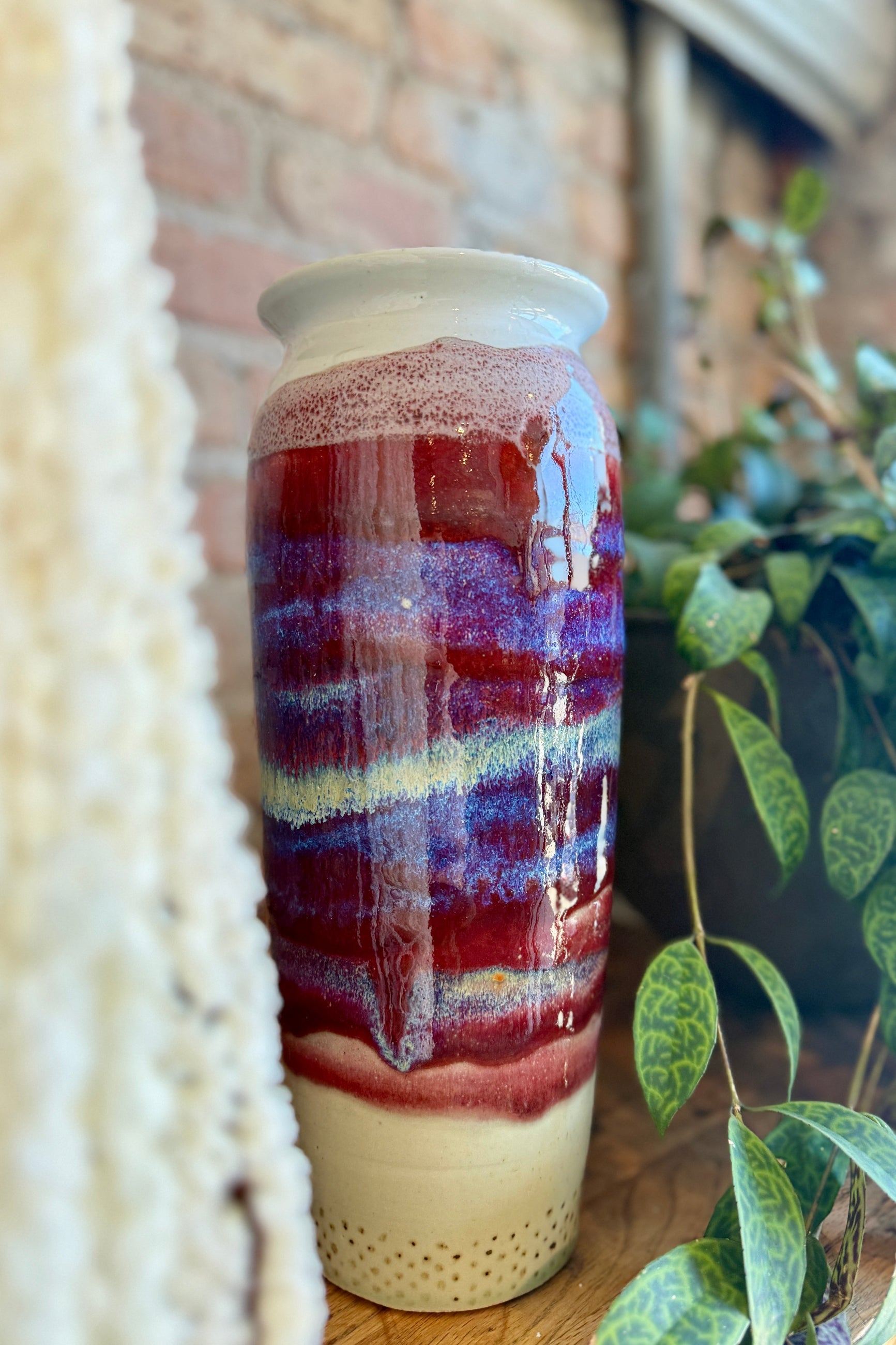 Decorative Bruning Pottery ceramic vase with multicolored glaze on a wooden surface with a plant in the background. ©Sprout Home