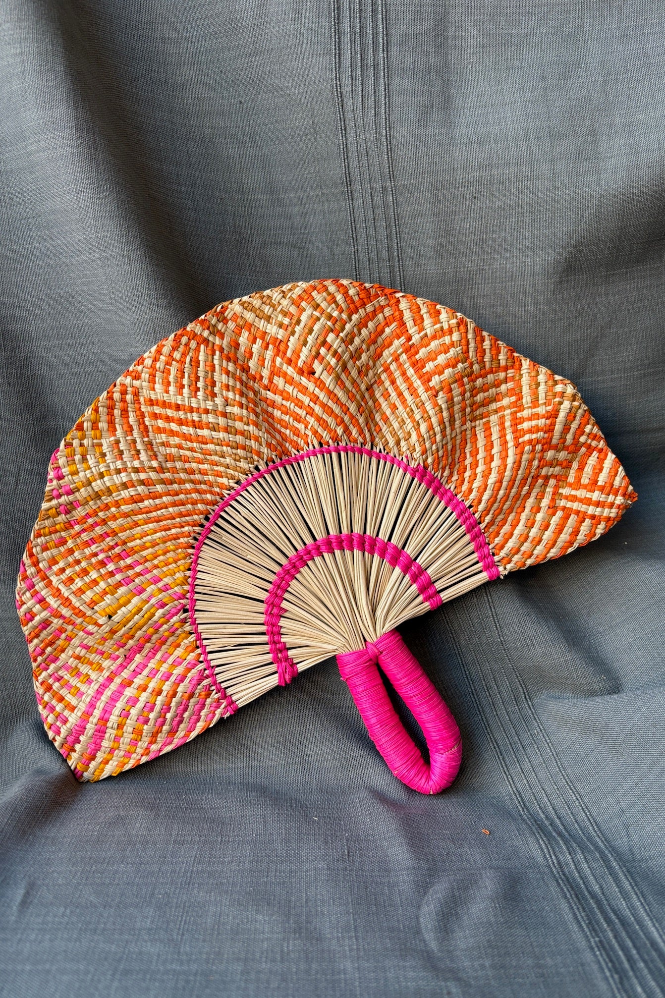 Toquilla Frilly Hand Fan Natural, Pink & Orange palm fiber and wire. A hand holds the fan in front of a grey backdrop