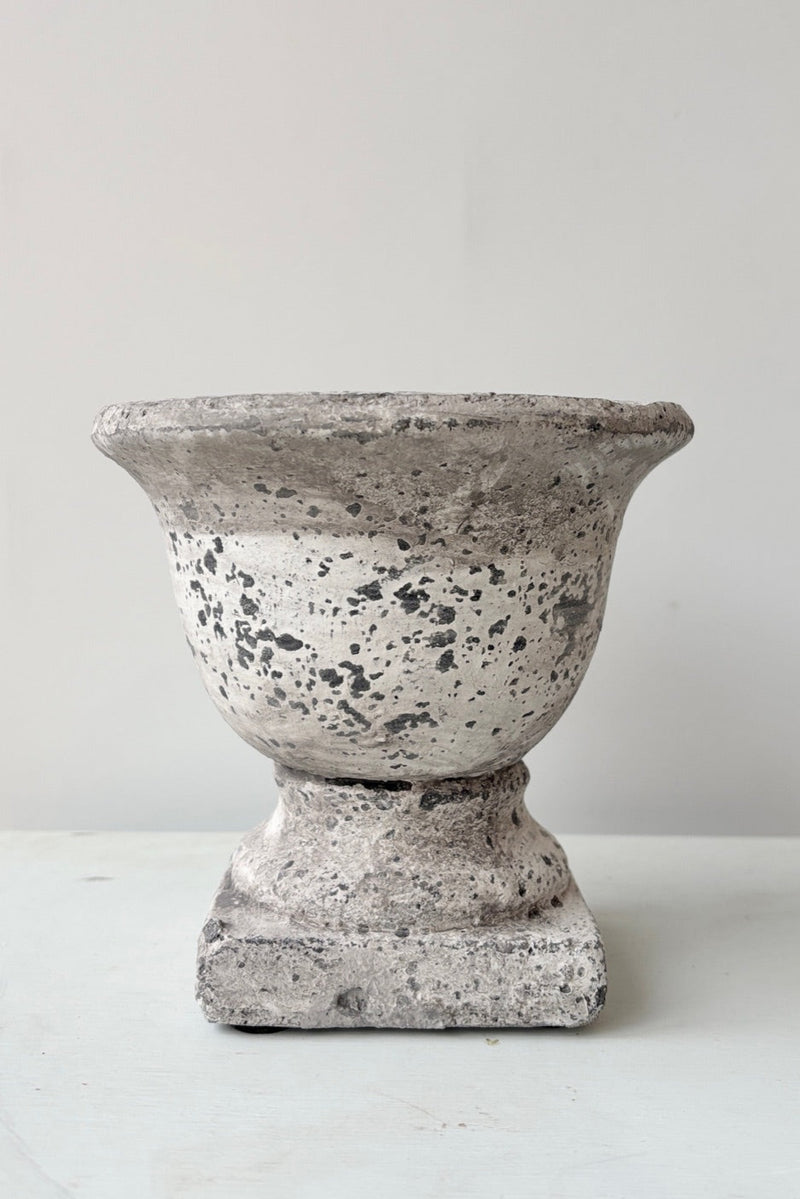 Small stone urn with a white and grey textured surface against a white wall. 