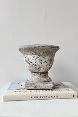 Small stone urn with a white and grey  textured surface displayed on a book against a white background.