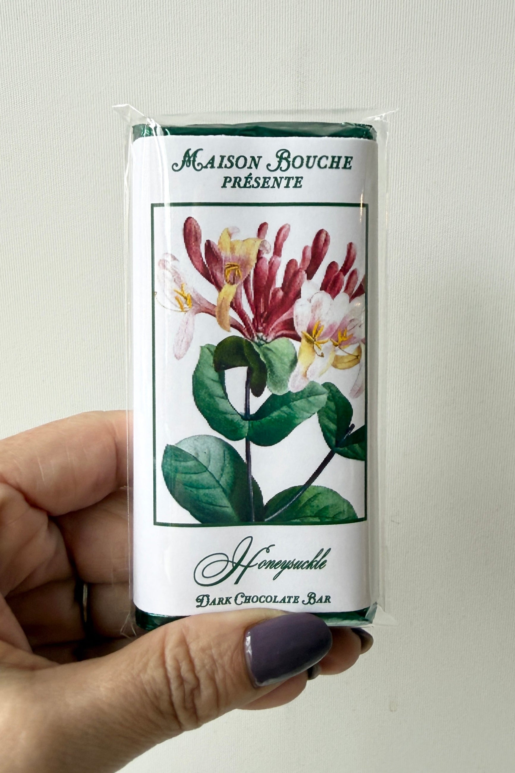 Hand holding a Maison Bouche honeyuckle dark chocolate bar packaging against a neutral background ©Sprout Home 