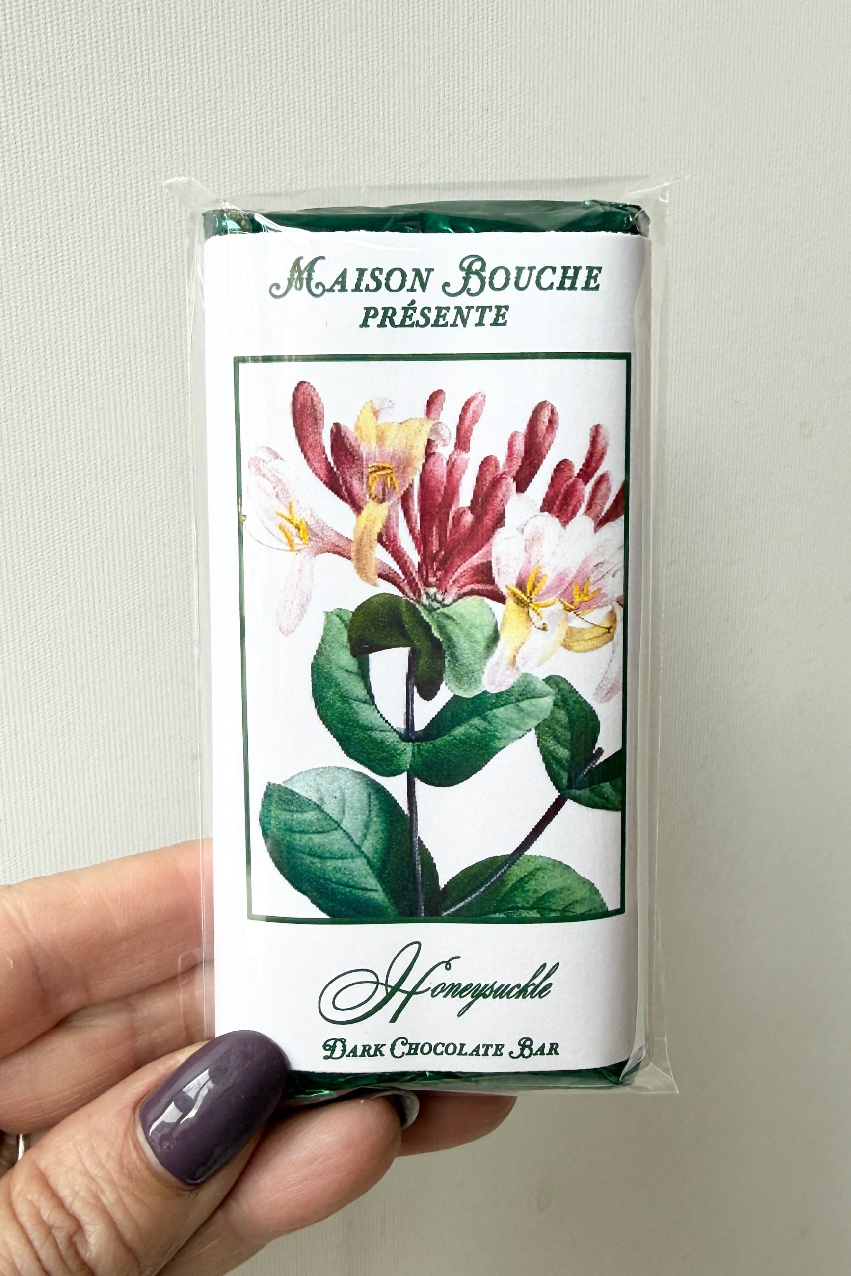 Hand holding a Maison Bouche honeyuckle dark chocolate bar packaging against a neutral background ©Sprout Home