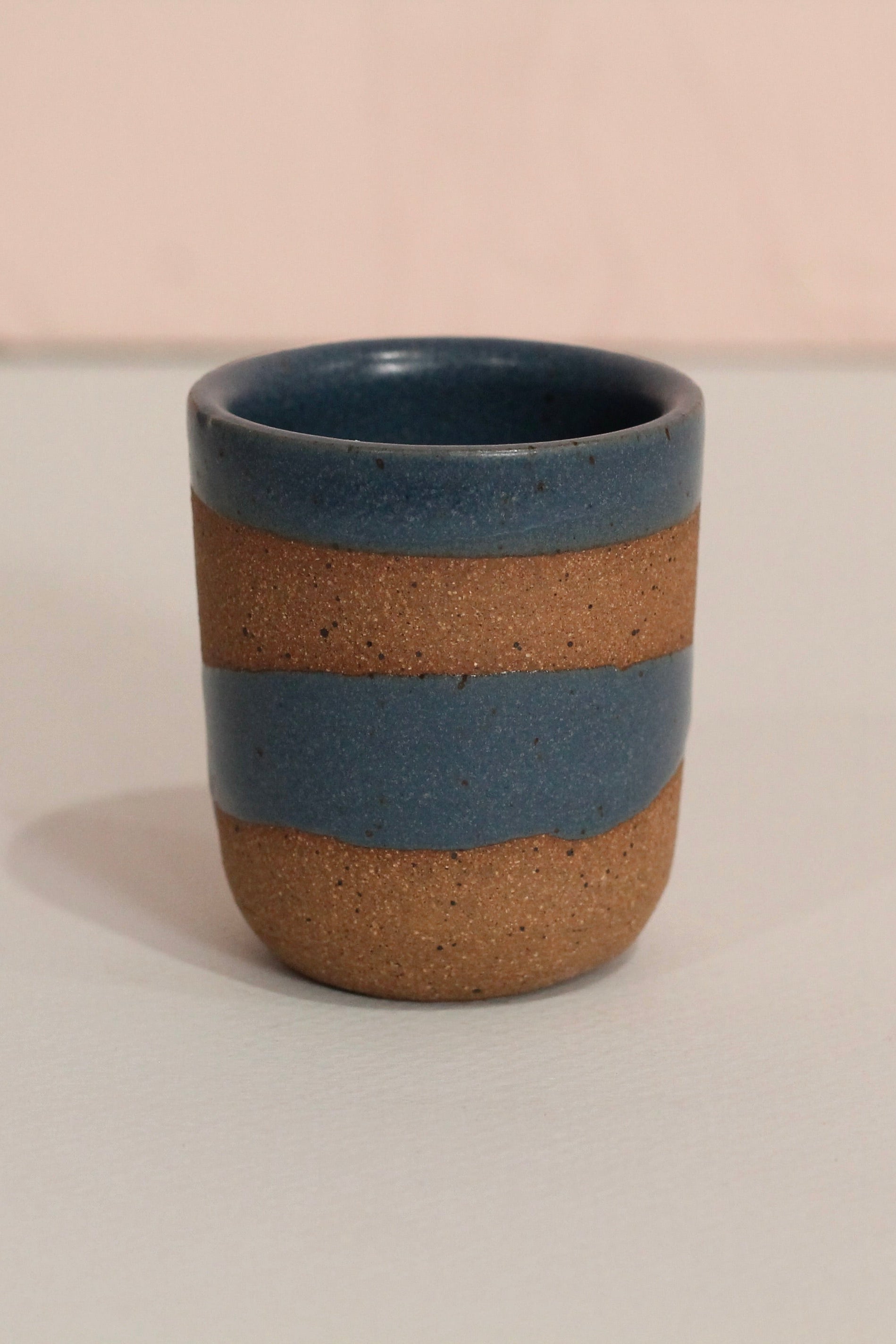 Ceramic cup with blue and brown stripes on a light background ©Christina Kosinski
