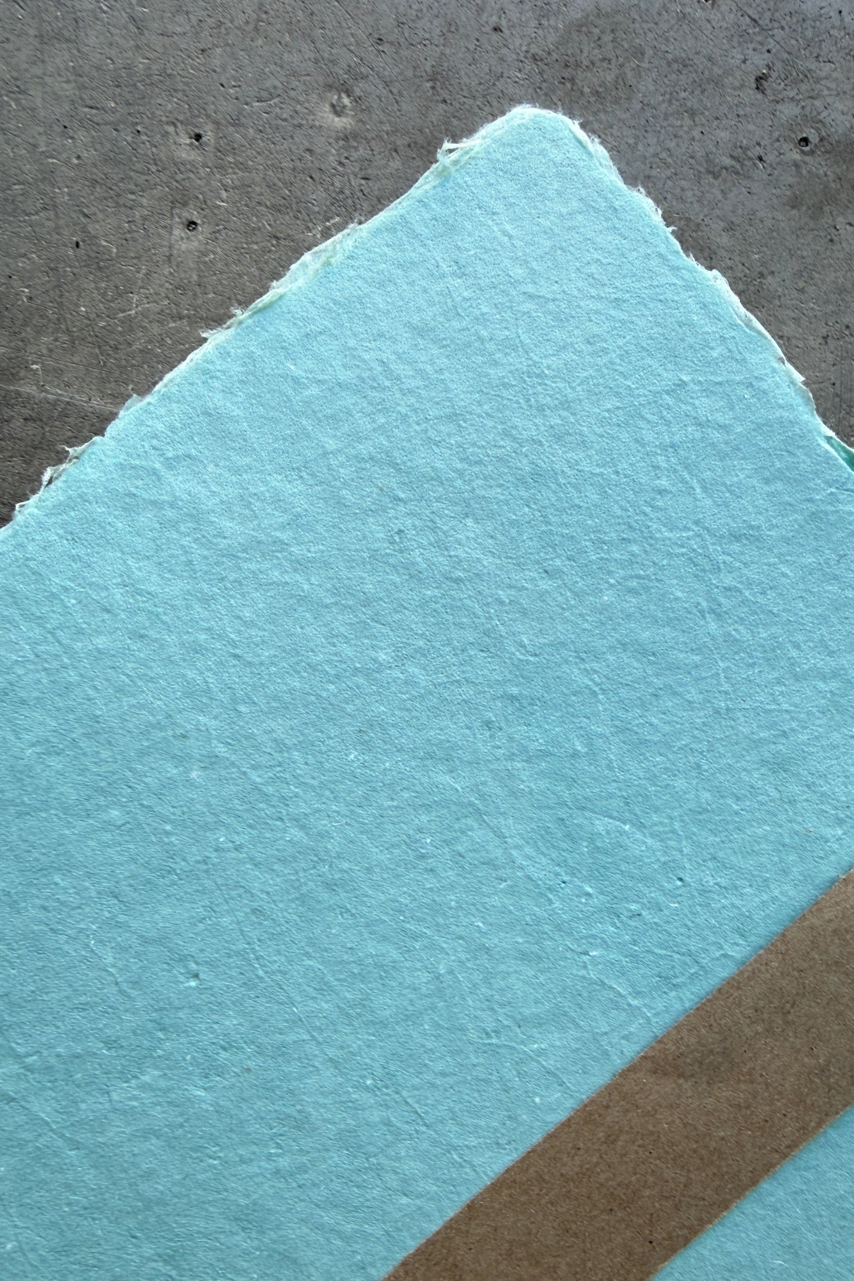 Close-up of a textured Handmade Celadon Paper Sheet Set in 8x10 by Sustainable Craft on a concrete floor ©Sprout Home