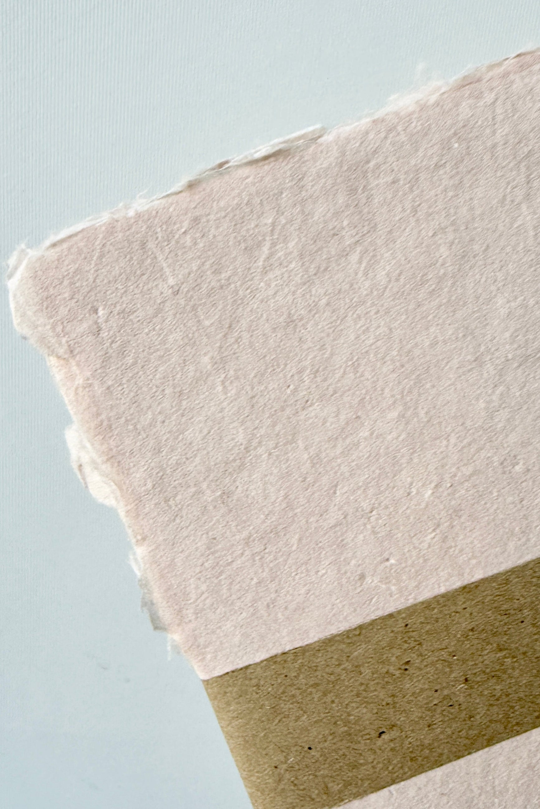 Close-up of Handmade Blush Paper Sheet Set in 5 x 7" by Sustainable Paper + Craft with textured surfaces on a light blue background ©Sprout Home