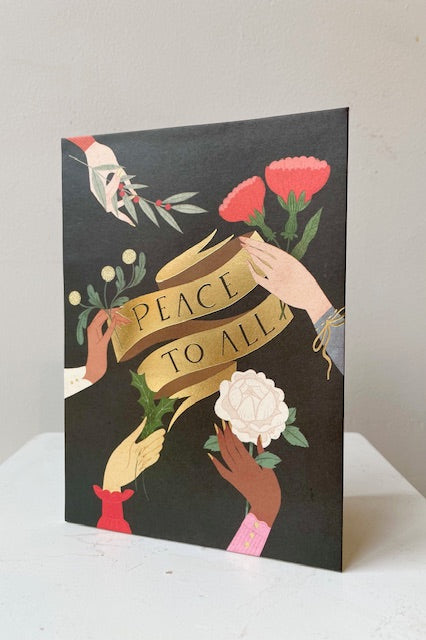 Front of pop up card with gold banner in the center and offering hands holding flowers on black background. Text says peace to all. 