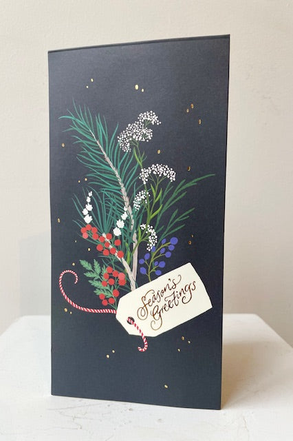 Front of pop up card with image of winter foliage and gift tag on black background. Text says Seasons Greetings. 