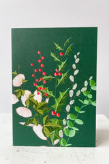 Bouquet of assorted Holiday stems on green background. Image of holly stems, pussywillow, boxwood, silver dollar. Blank inside. 