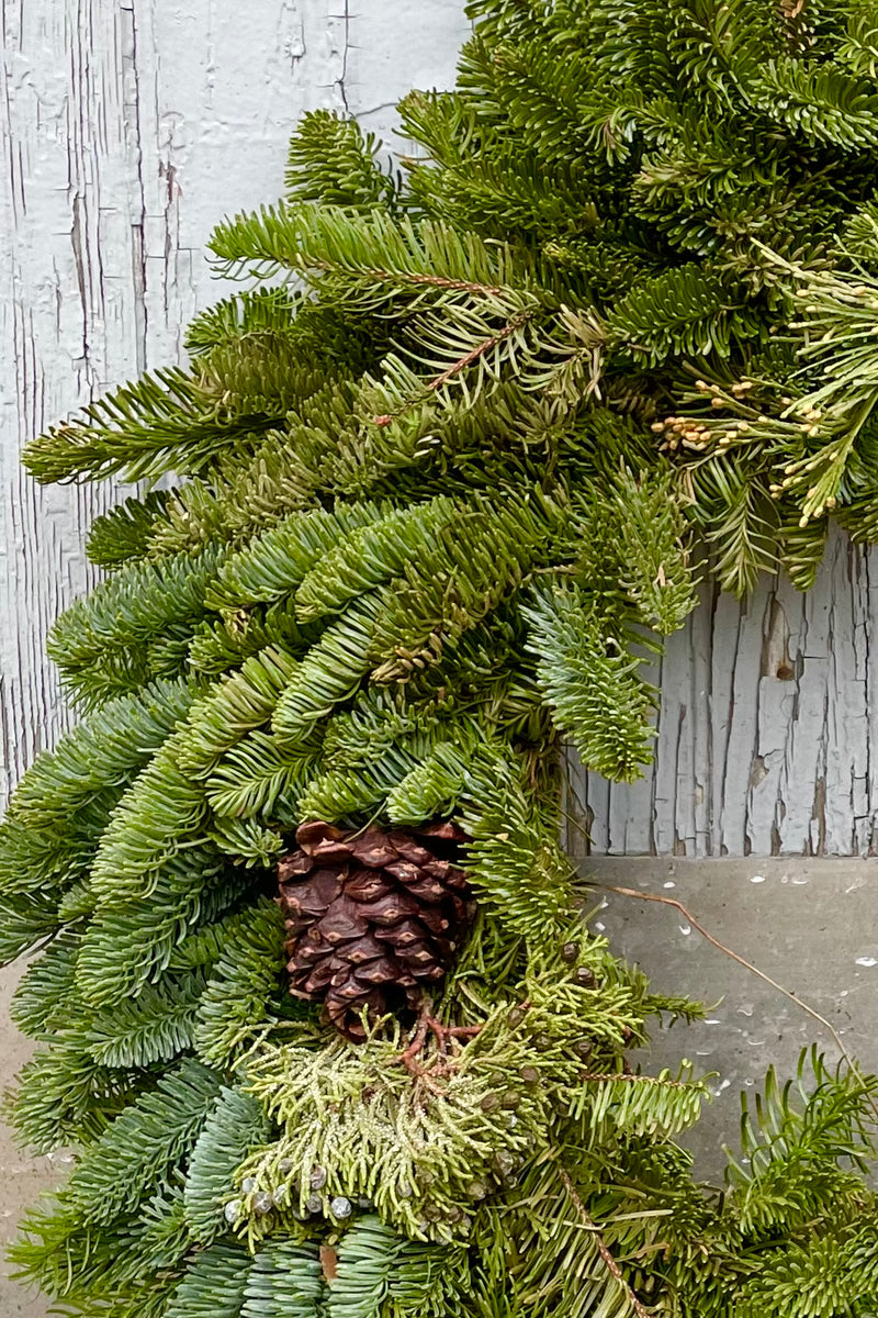 Close up of Holiday Masterpiece wreath with green fir and pinecones against grey wall