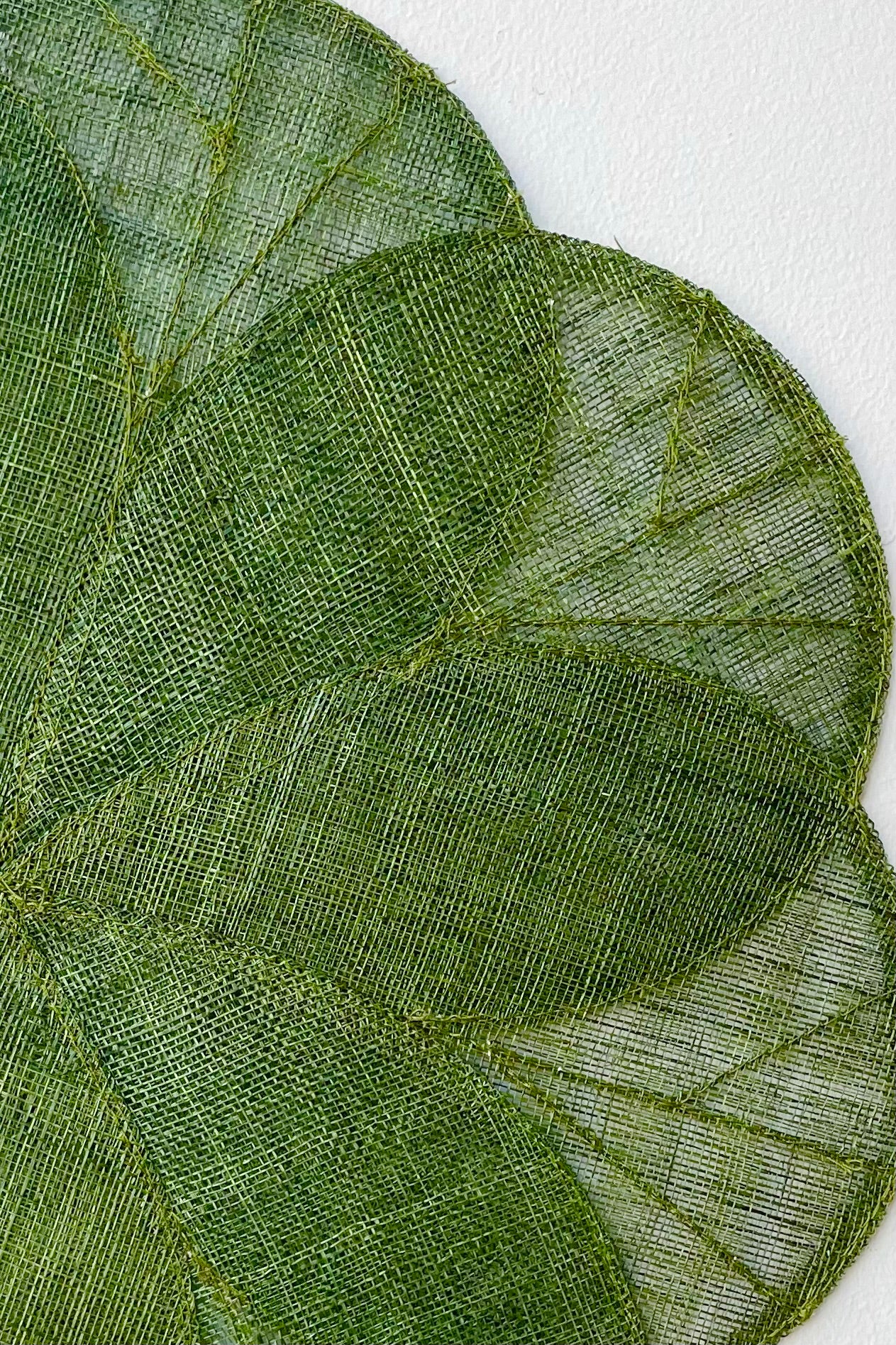 Close up of Sheer woven dark green placemat in flower design against white wall