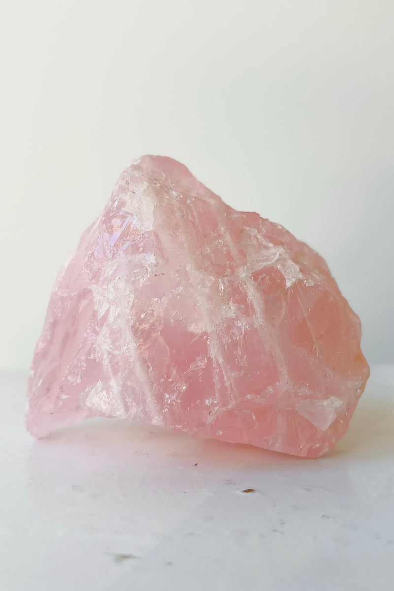 Rose quartz crystal on white surface in front of white background