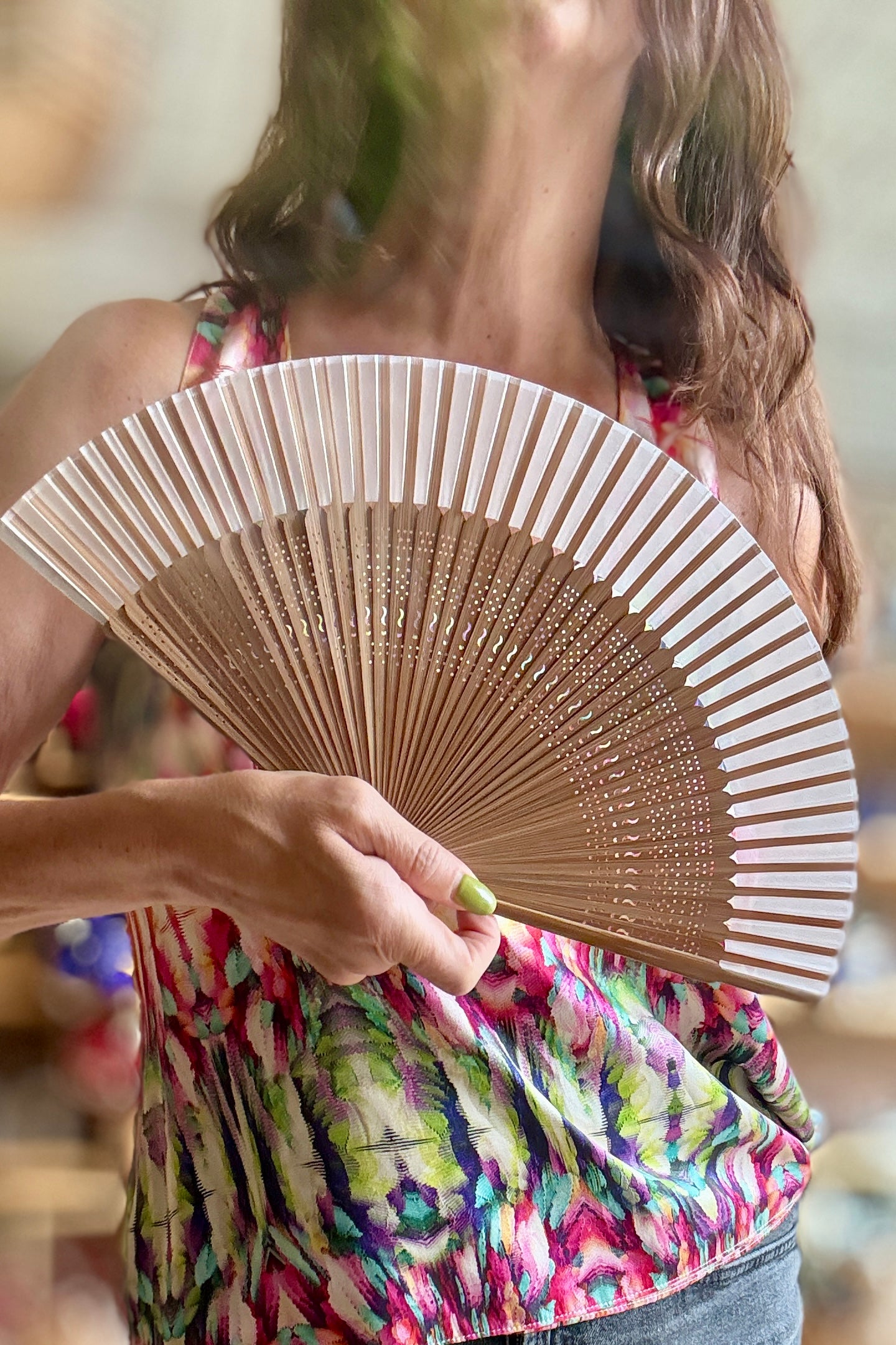 A woman holding a traditional folding Silk Folding Fan Light Beige w/ Brown Bamboo made of light-colored wood or bamboo, wearing a colorful floral print top. ©Sprout Home