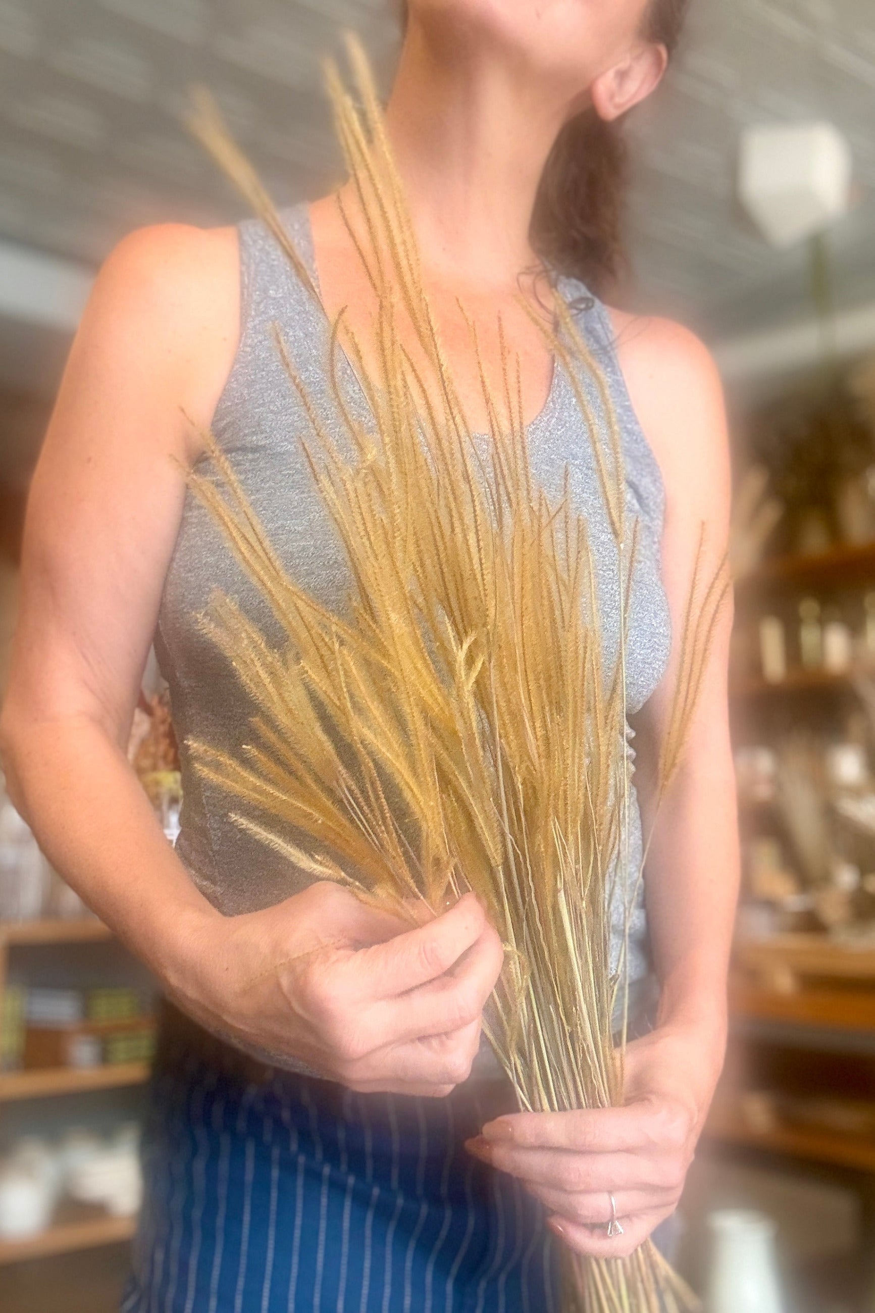 A woman in a gray sleeveless top and blue pinstriped apron holds a Ouro Natural Preserved Bunch in a shop setting. ©Sprout Home