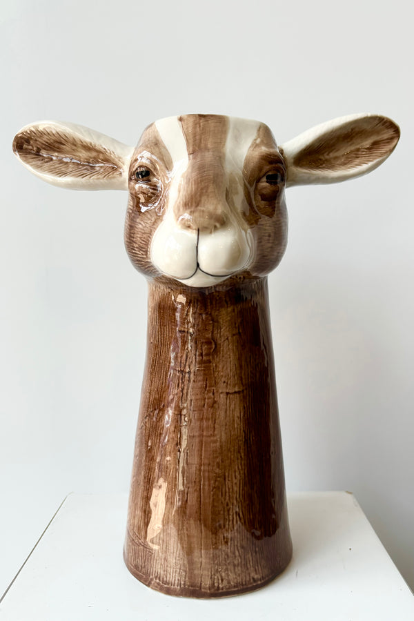 Front view of a ceramic vase in the shape of a brown and white goat head against white background.