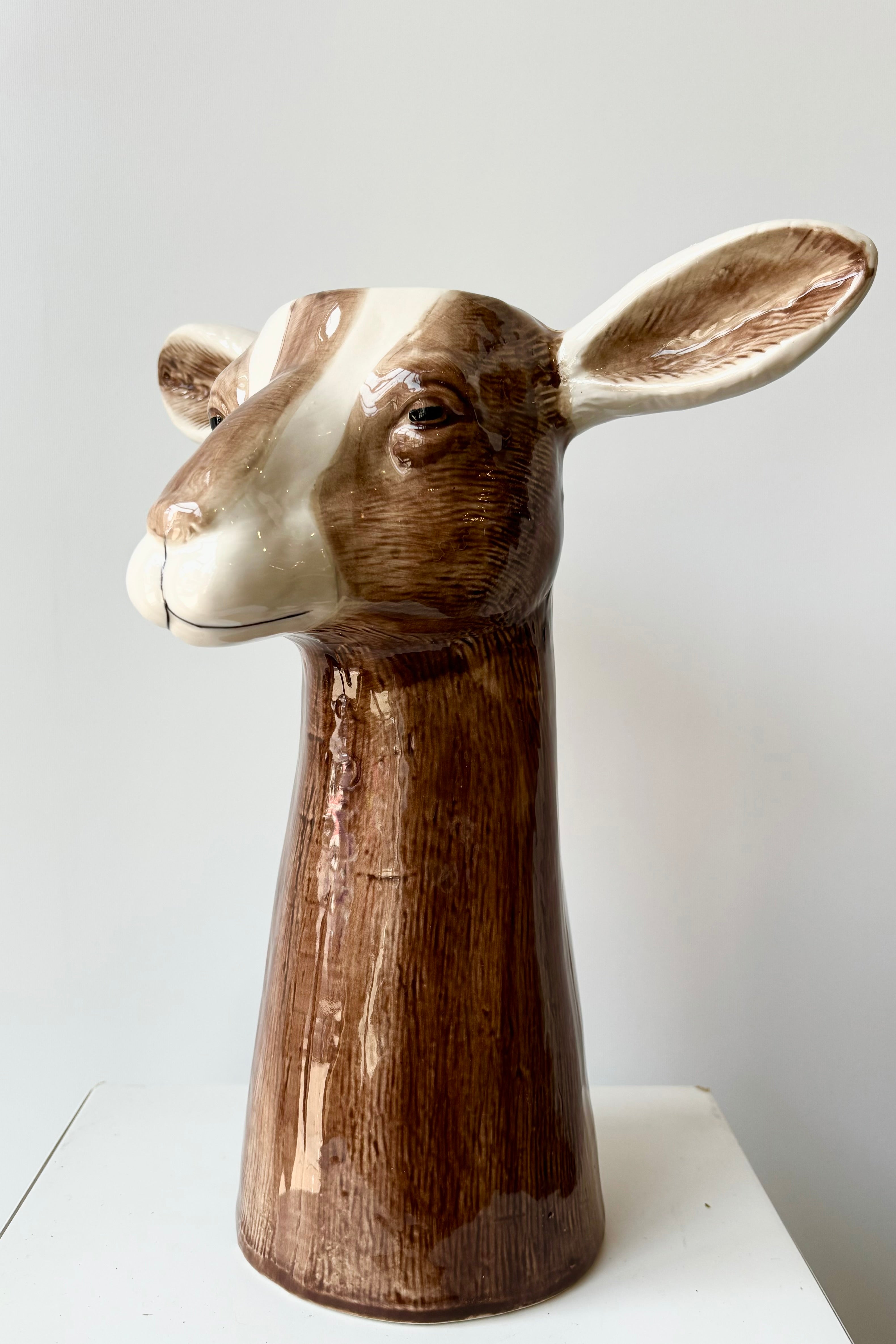 Side view of a ceramic vase in the shape of a brown and white goat head against white background.