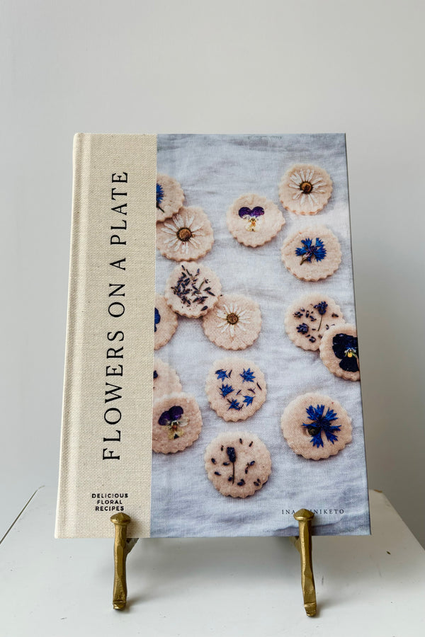 Front cover of 'Flowers on a Plate' Book showing several sugar cookies decorated with dried flowers in a gold bookstand against a white background