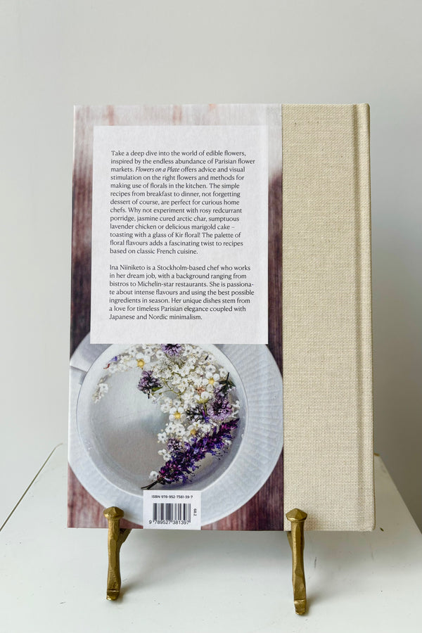 Back cover of 'Flowers on a Plate' Book showing the book description and a photo of a plate with dried flowers on it, displayed in a gold bookstand against a white background