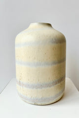 Ceramic bud vase with cream colored glaze with stripes of grey throughout against white background