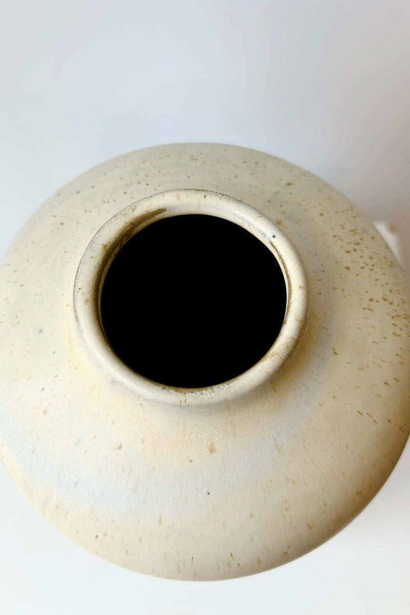 Opening of ceramic bud vase with cream colored glaze with stripes of grey throughout against white background